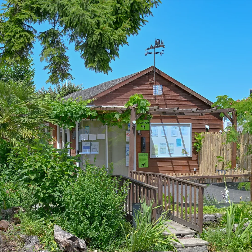 Chalet d'accueil en bois avec girouette et panneaux d'information du camping à Pontaubault