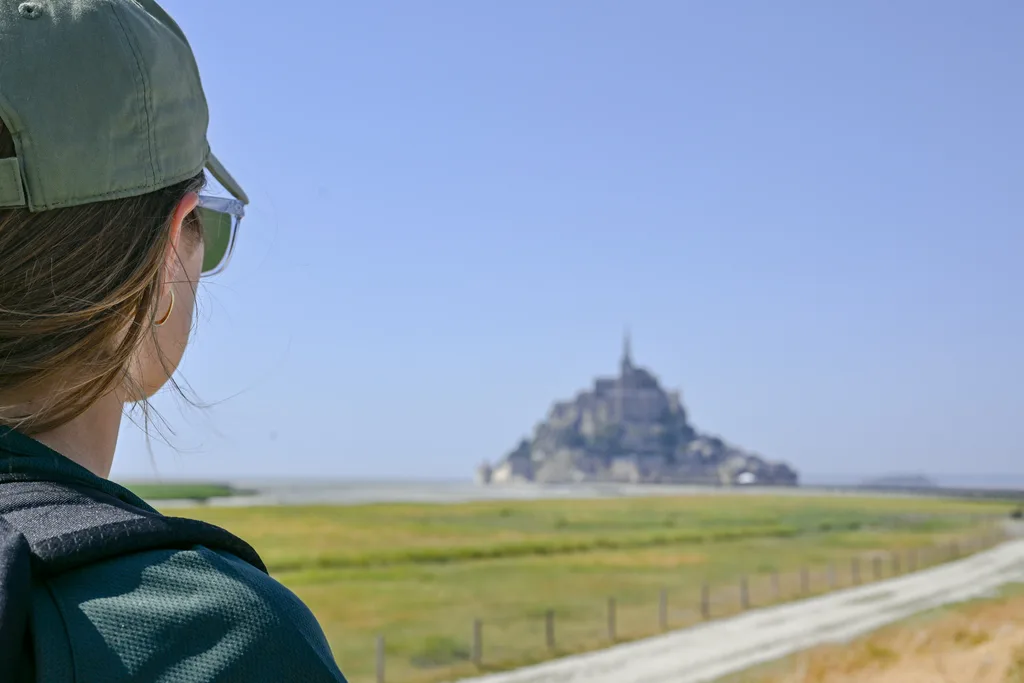 Visiteuse en casquette contemplant la silhouette du Mont-Saint-Michel dans la baie venant du Parking Mont-Saint-Michel